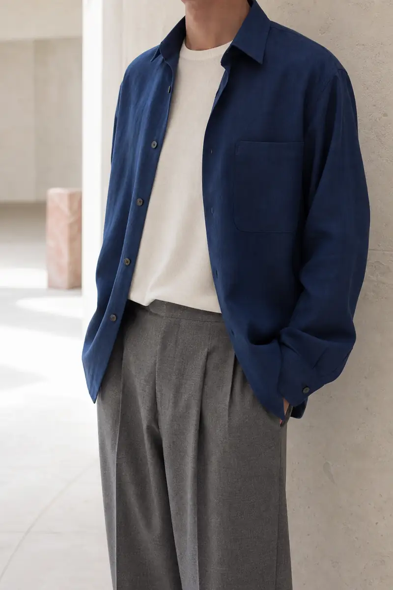 Uomo con sopracamicia blu, t-shirt in maglia avorio e pantaloni grigi con pinces